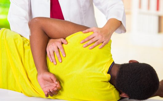 Man lying down getting physical shoulder treatment from physio therapist, patient looking into camera while her hands working on his upper arm area, medical concept.